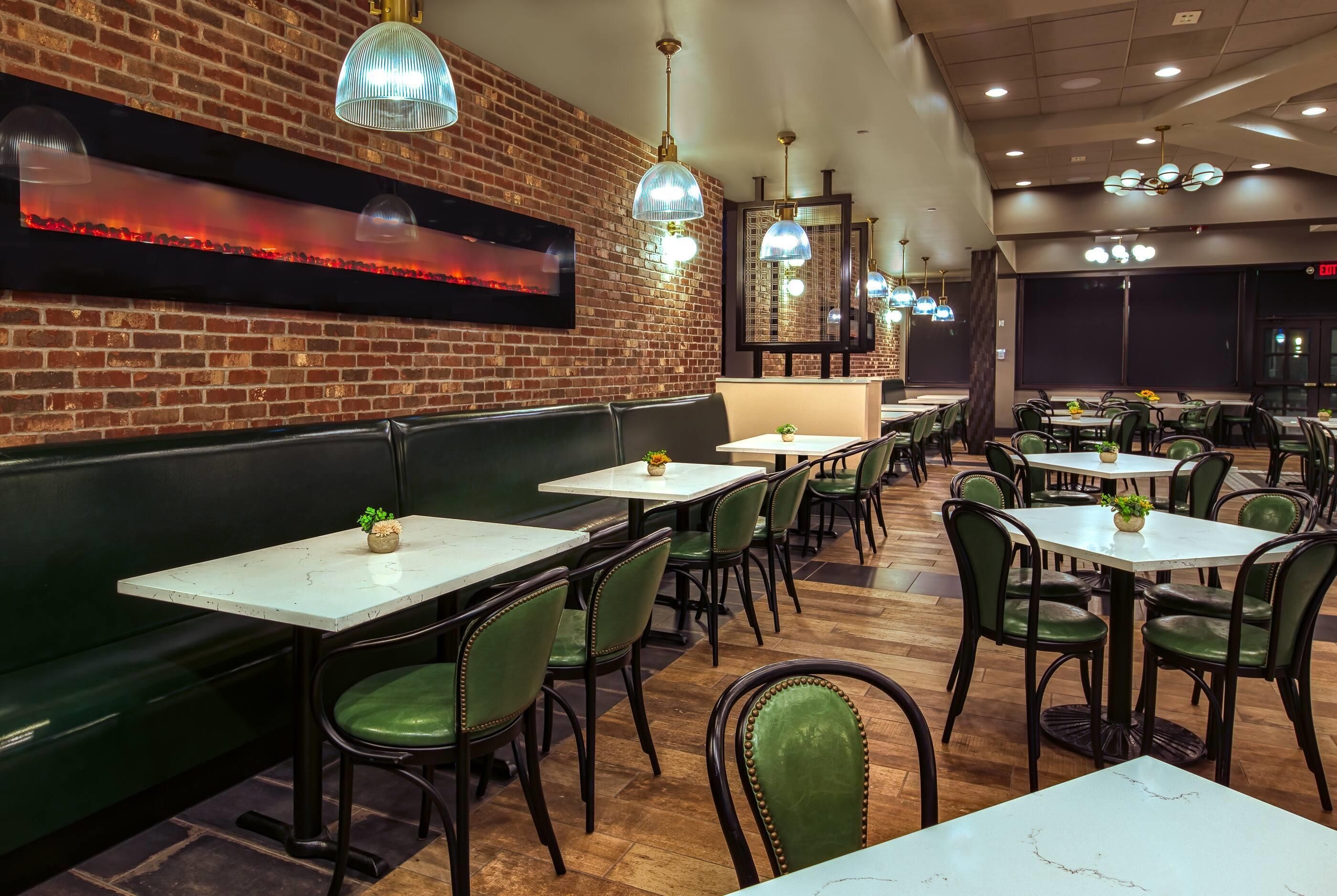 Interior de restaurante con paredes de ladrillo, varias mesas y cabinas, sillas verdes e iluminación colgante.