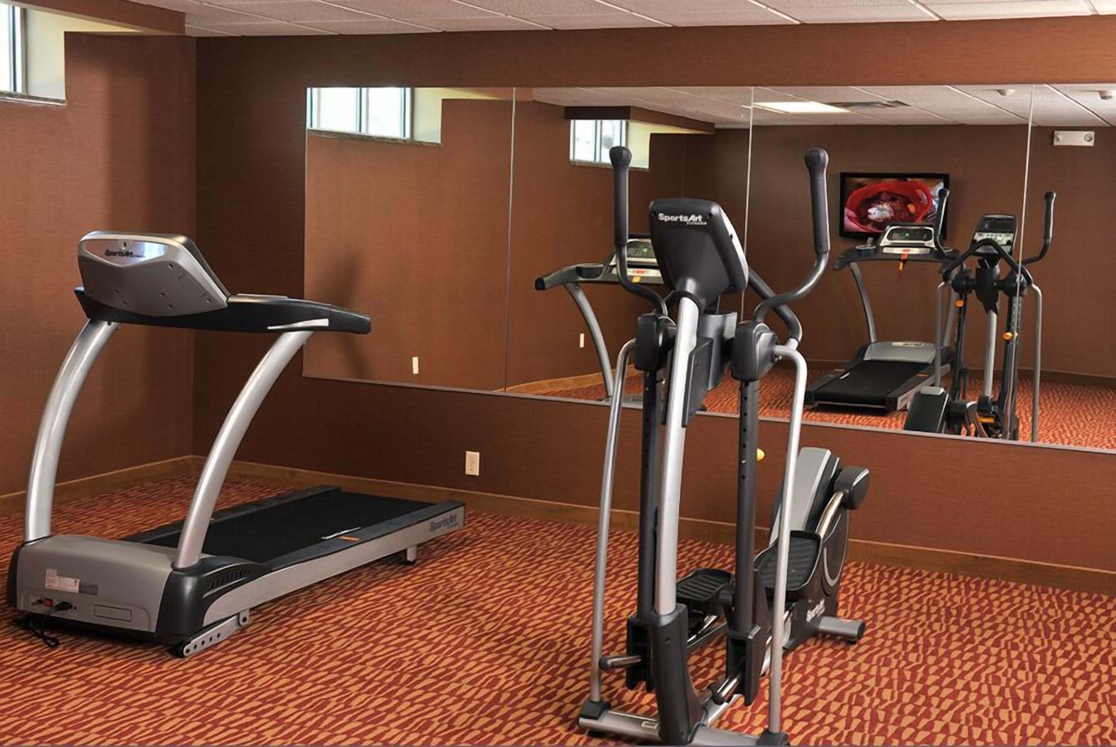 A gym with treadmills, ellipticals, and a mirrored wall.