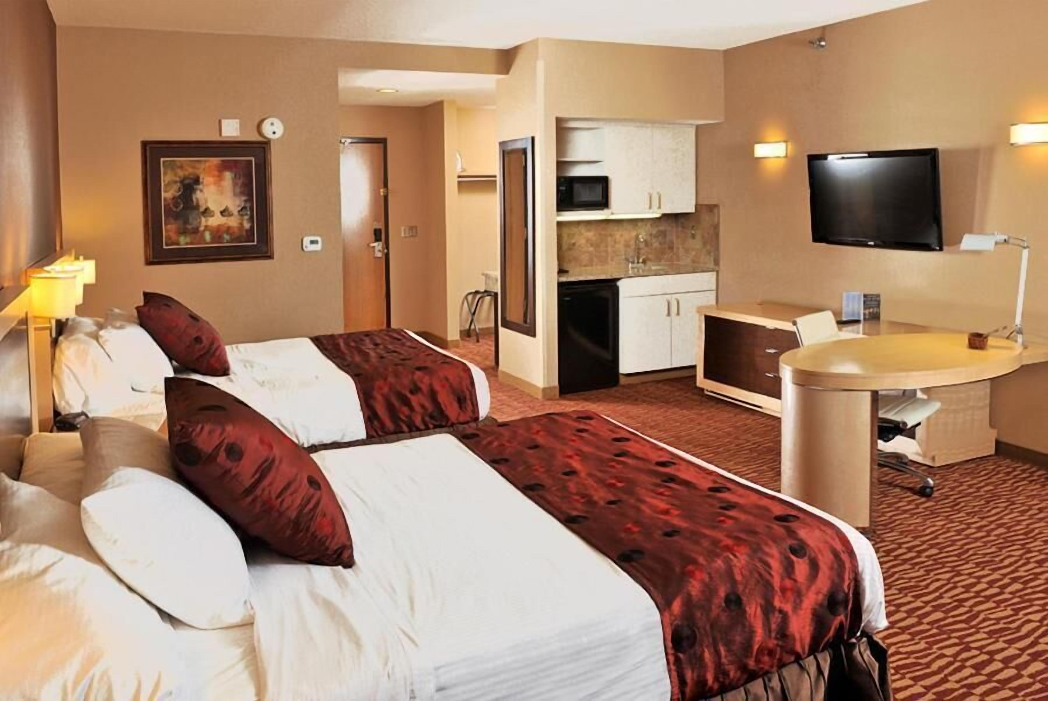 Habitación de hotel con dos camas, una kitchenette, un televisor y un escritorio con silla.