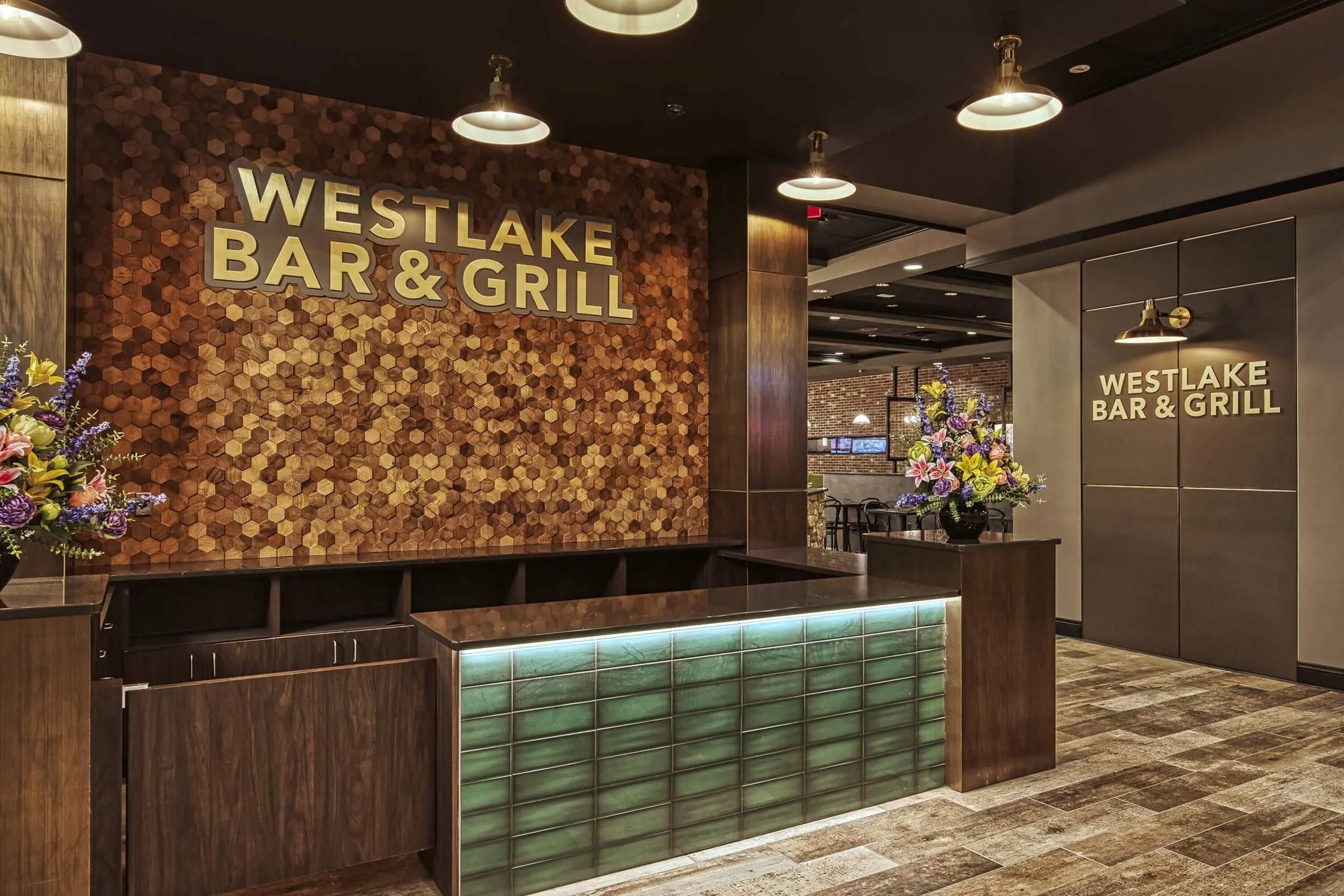 A reception area with a wooden hexagonal wall design and a sign reading 'WESTLAKE BAR & GRILL'.