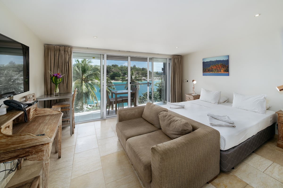 Habitación de hotel con una cama grande, un escritorio, una silla y vistas a una piscina y palmeras.