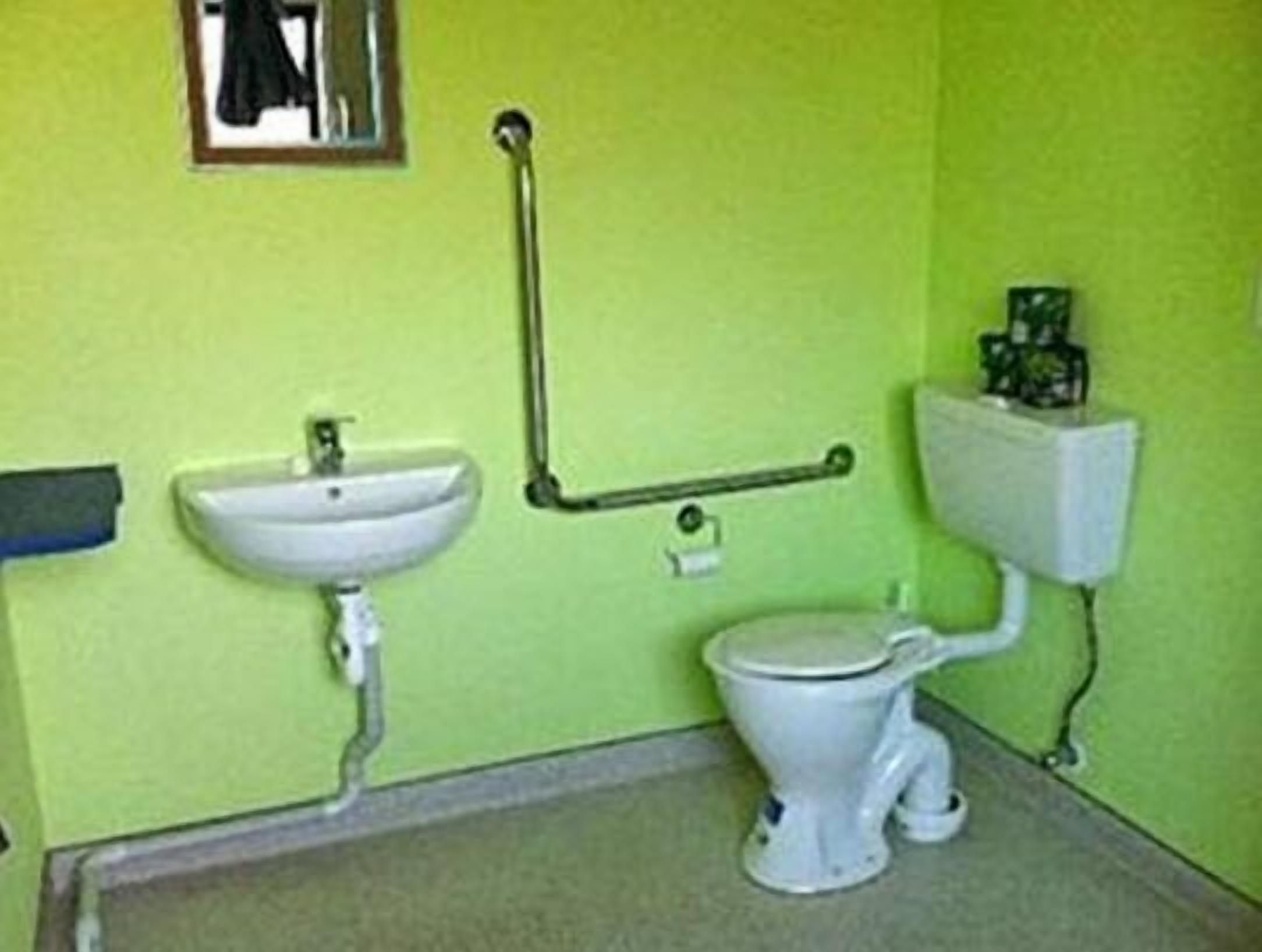 A small bathroom with a sink, toilet, and a handrail.