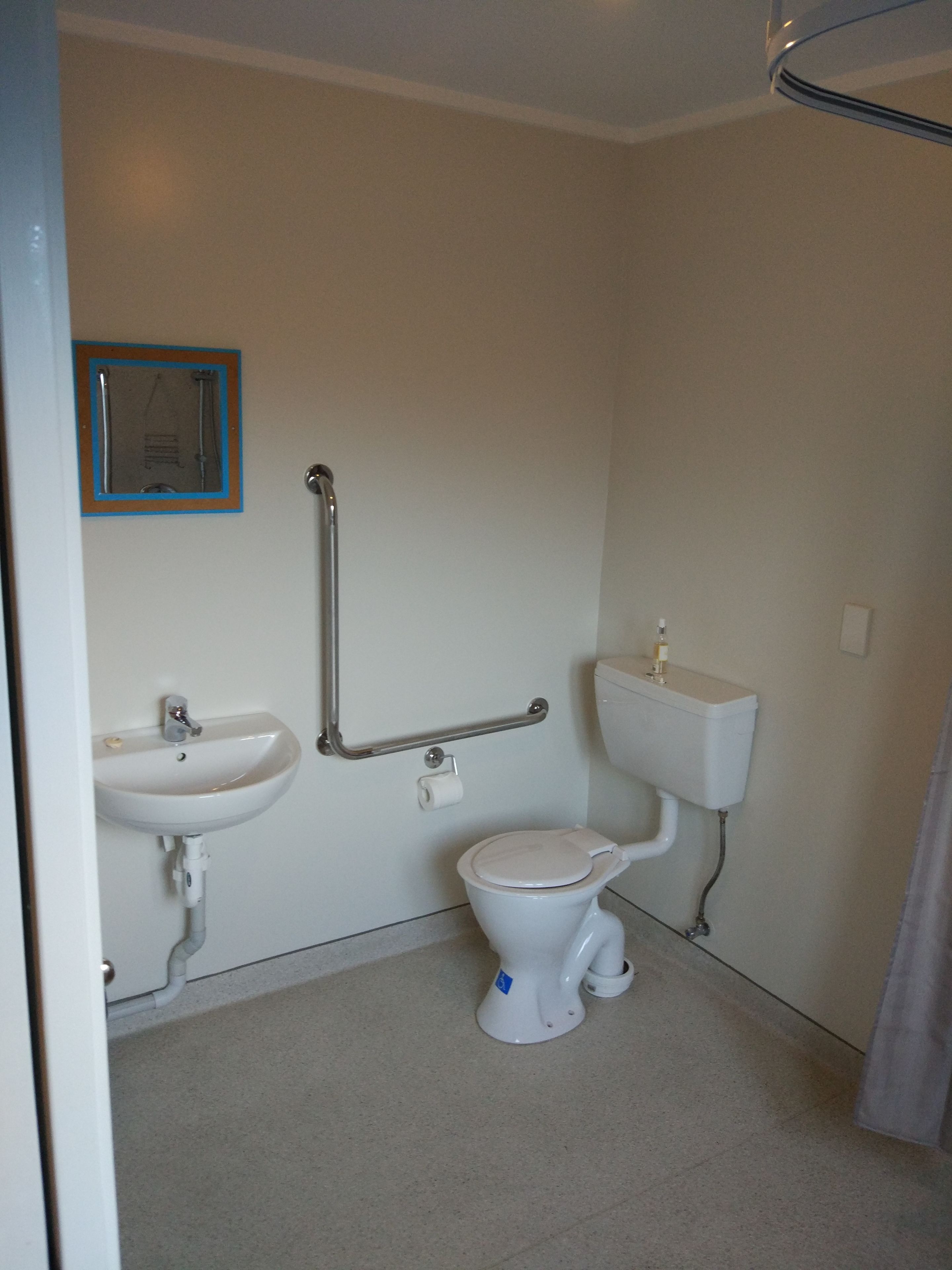 A small, clean bathroom with a toilet, sink, and grab bars.