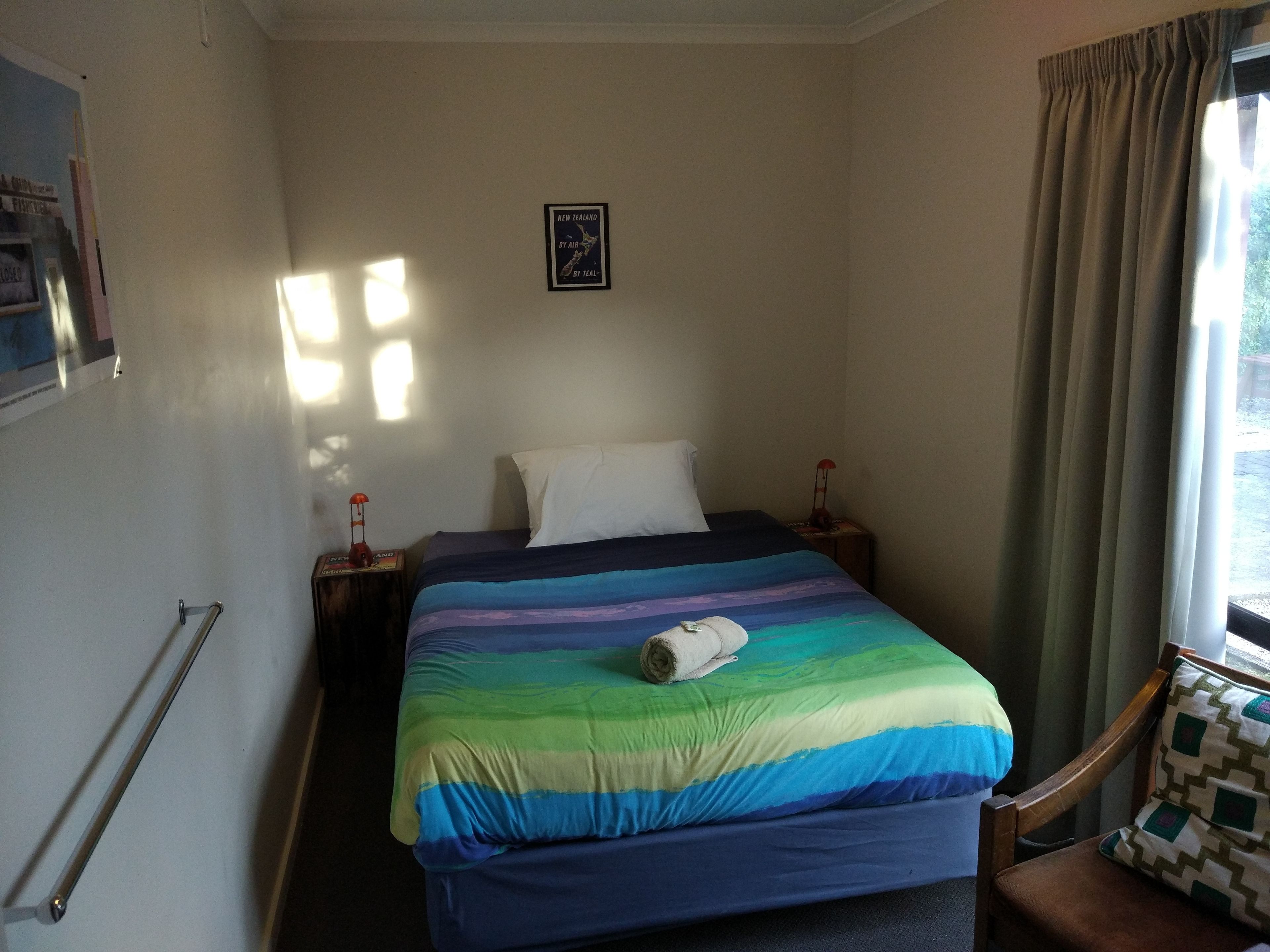 Una cama individual con un edredón de colores, una mesita de noche con una lámpara, un mapa enmarcado en la pared y una ventana con cortinas.