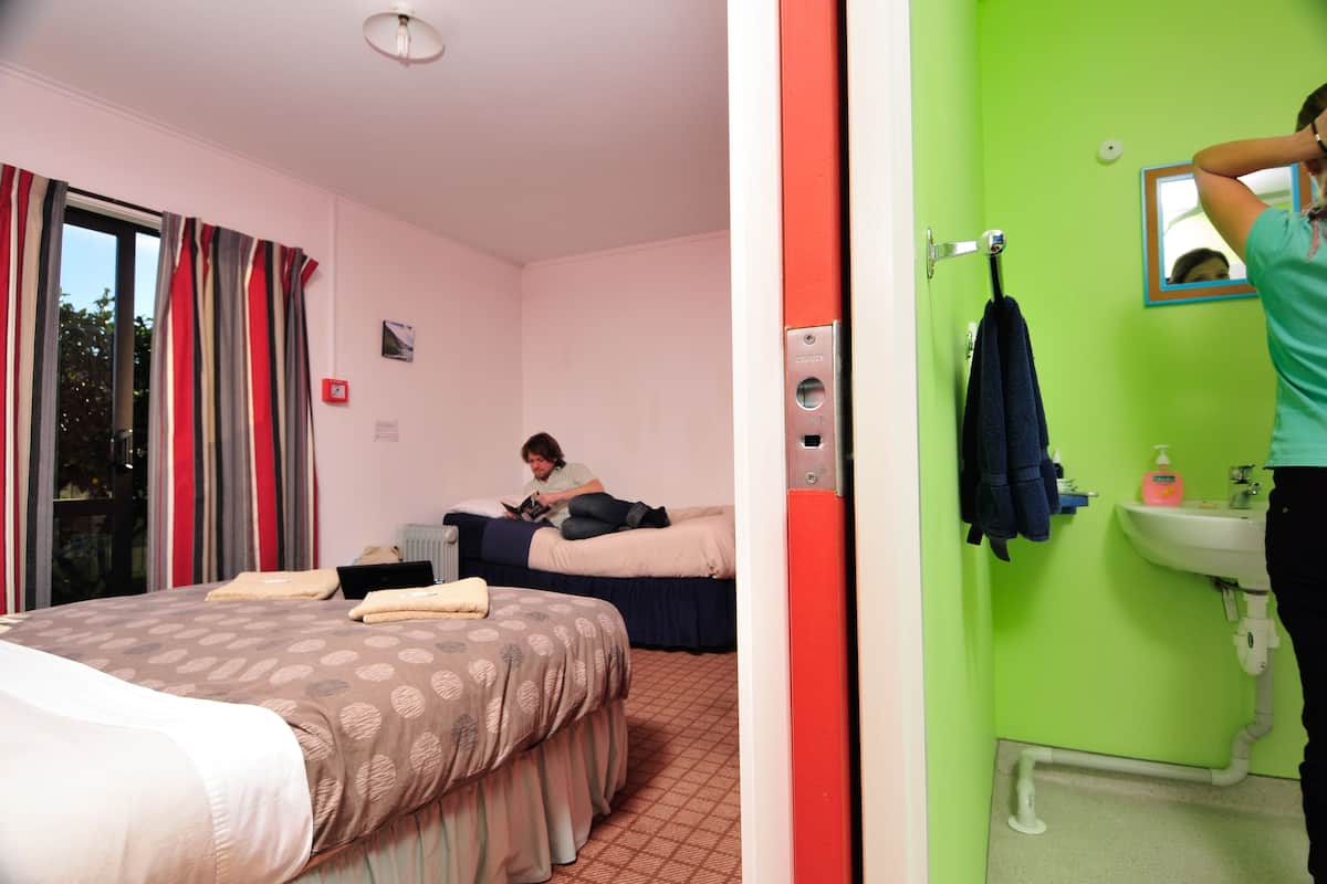 Une chambre d’hôtel comprenant un lit, un coin lecture, une fenêtre avec des rideaux et une salle de bain avec un lavabo et un miroir.