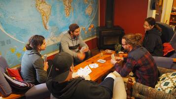 A group of people playing cards around a wooden table in a room with a large world map on the wall.