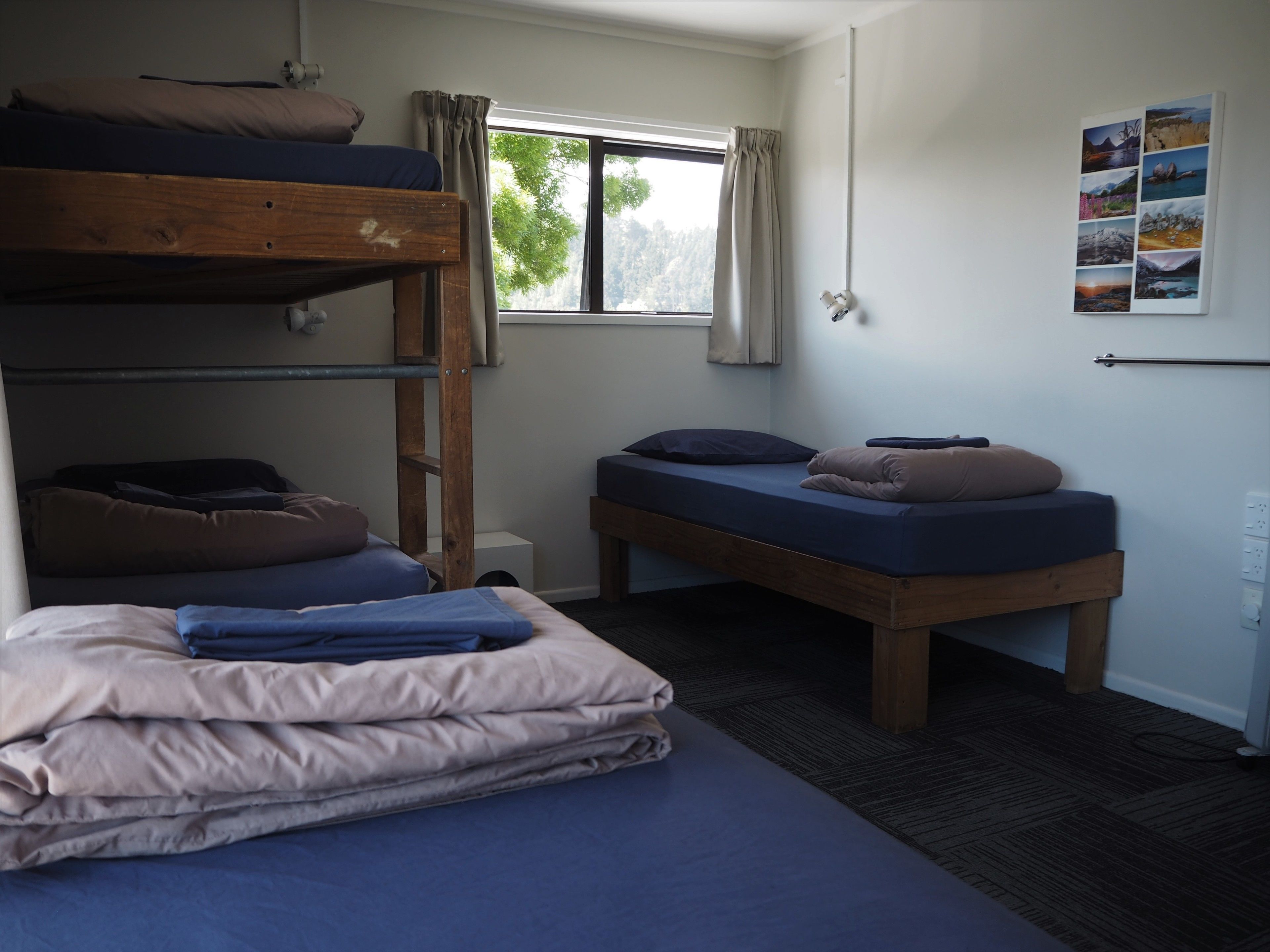 Een slaapzaal met stapelbedden, een eenpersoonsbed, een raam met gordijnen en een radiator aan de muur.