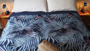 A bed with a blue and white leaf-patterned bedspread, two white pillows, and a folded brown towel.