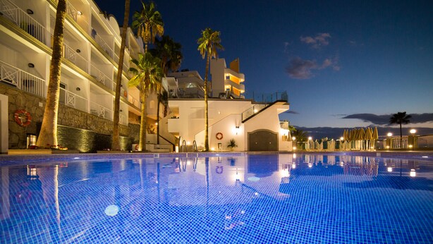 A hotel pool with a clear blue tiled surface, palm trees, and a modern building with balconies. - Apartamentos Cala D'Or (Mogan)