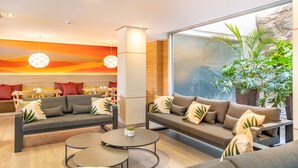 A modern lounge area with sofas, a coffee table, and a large window with a view of a rock wall and plants. - Apartamentos Cala D'Or (Mogan)