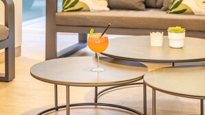 A modern indoor setting with a round table, a glass of drink, a sofa with patterned cushions, and a potted plant. - Apartamentos Cala D'Or (Mogan)