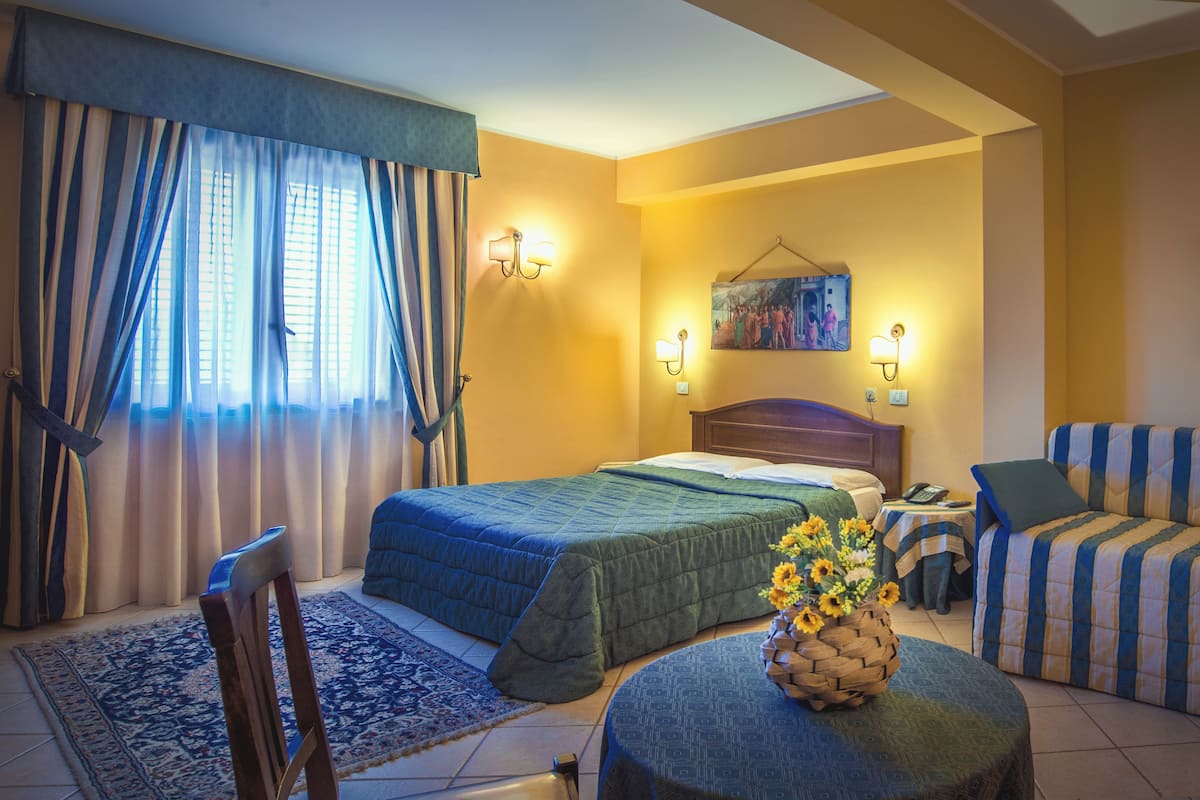 Une chambre d’hôtel avec un lit, un canapé, une chaise, une petite table et un tableau au mur.