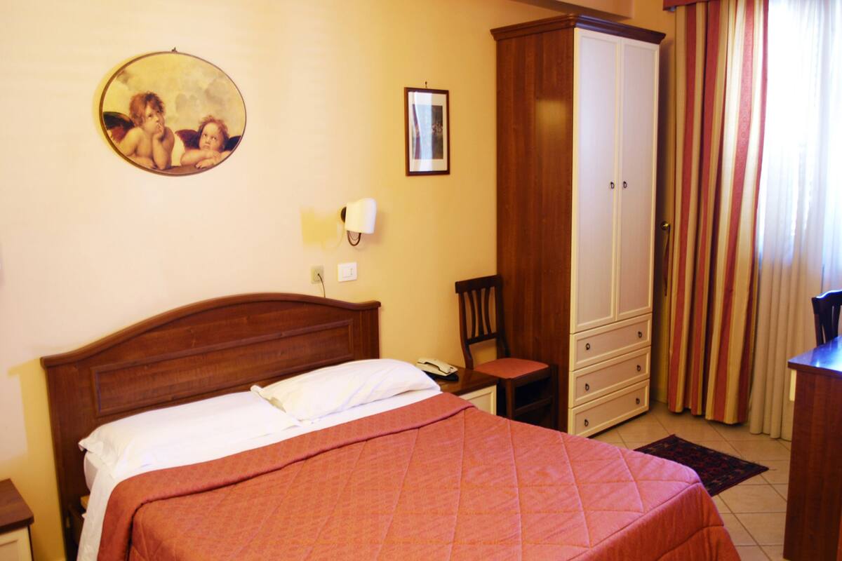 Une chambre à coucher avec un grand lit, une armoire en bois, une chaise et un tableau accroché au mur.