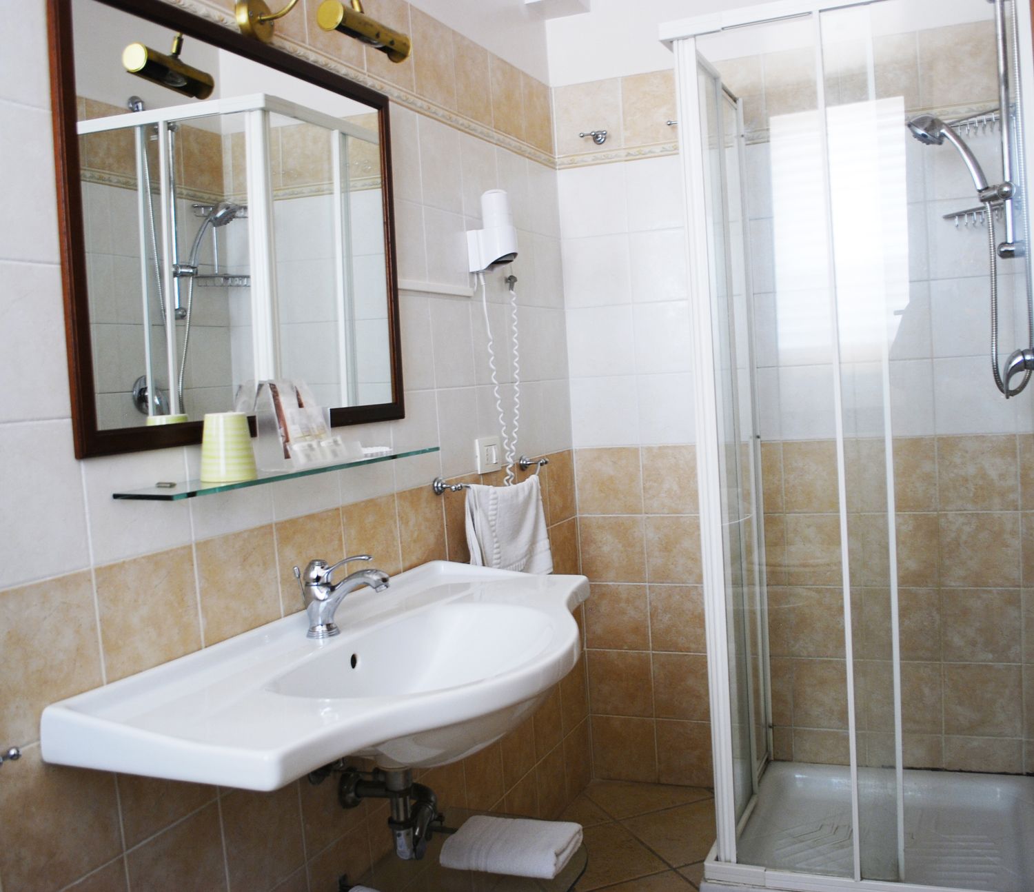 Un baño con lavamanos blanco, cabina de ducha de vidrio y espejo con marco dorado.