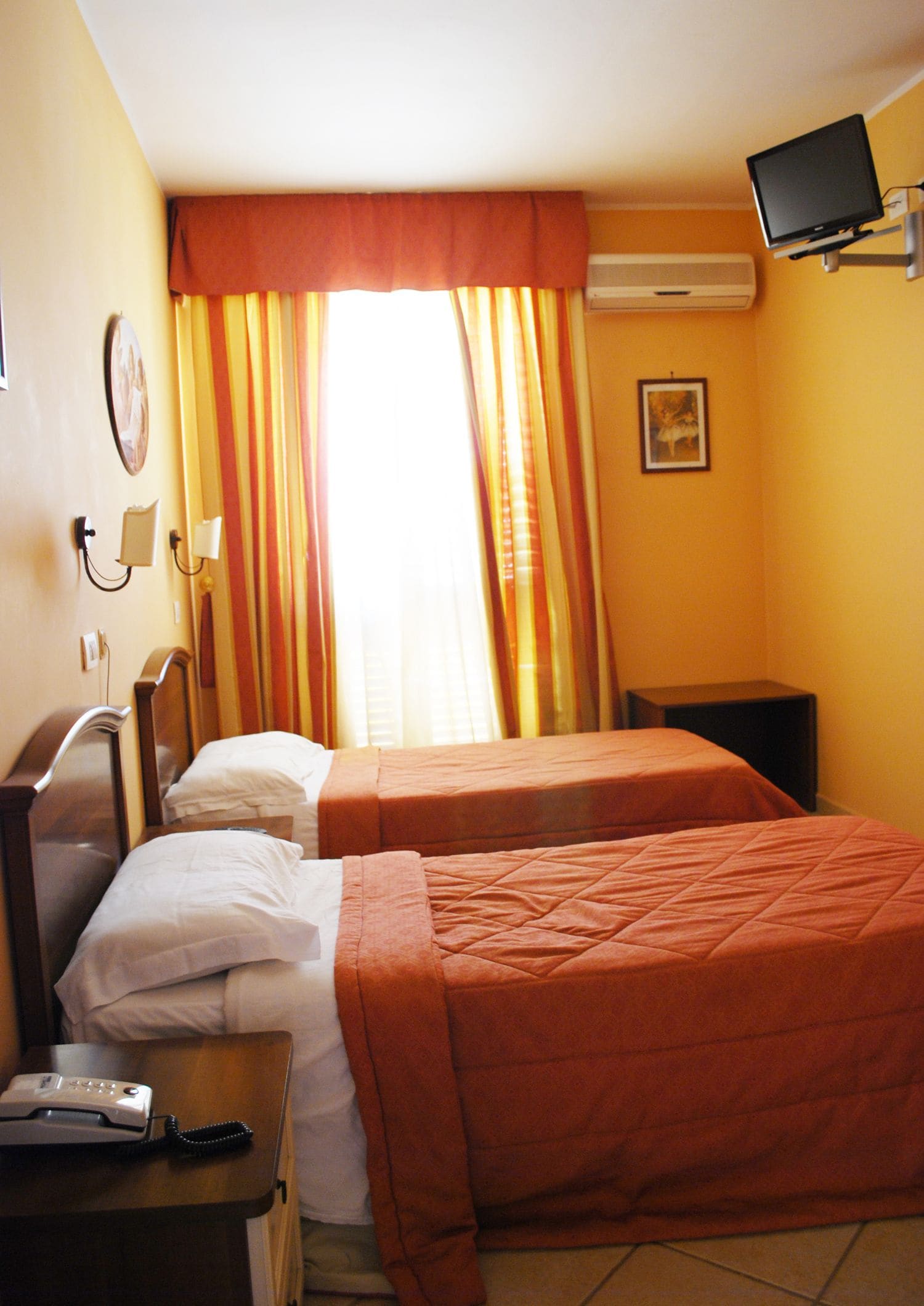 A hotel room with two beds, a TV, an air conditioner, and a telephone on a nightstand.