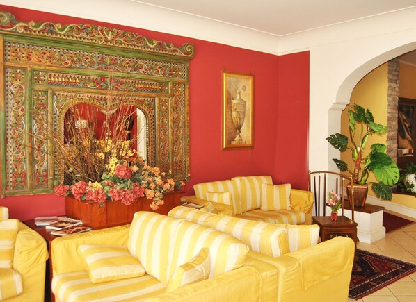 A living room with yellow-striped sofas, a large decorative mirror, and a potted plant.