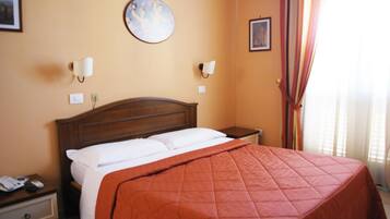 Quarto de hotel com uma cama grande, cabeceira de madeira, duas mesas de cabeceira, um criado-mudo e uma decoração redonda na parede, além de uma janela com cortinas.