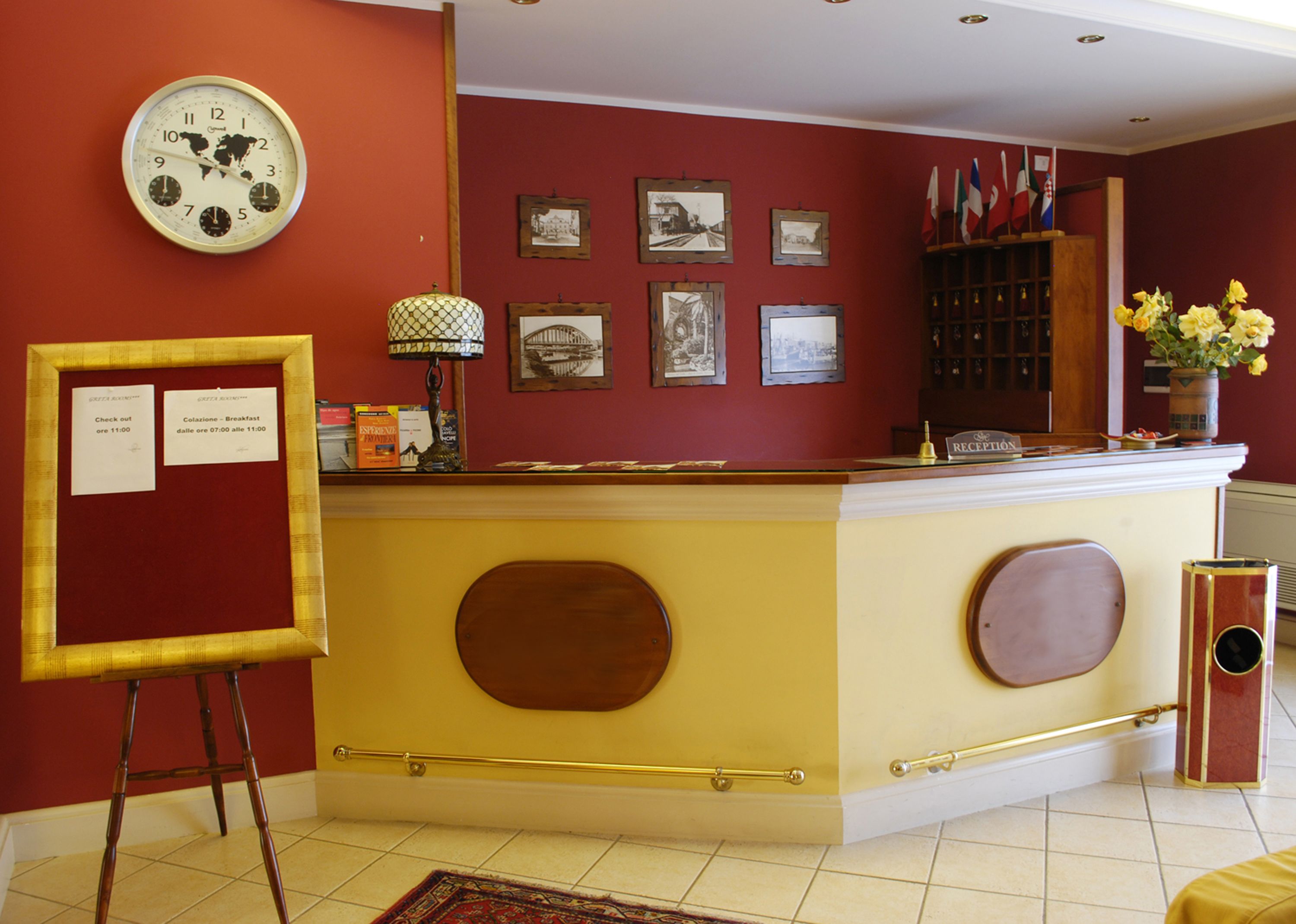 Un comptoir d’accueil avec une horloge, des tableaux encadrés et des drapeaux accrochés au mur.
