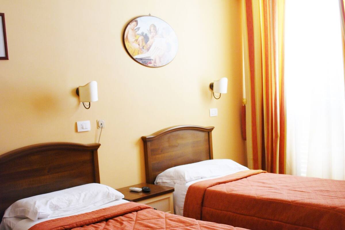 Une chambre d’hôtel avec deux lits, chacun doté d’une tête de lit en bois, d’une horloge murale ronde et de deux lampes de chevet.
