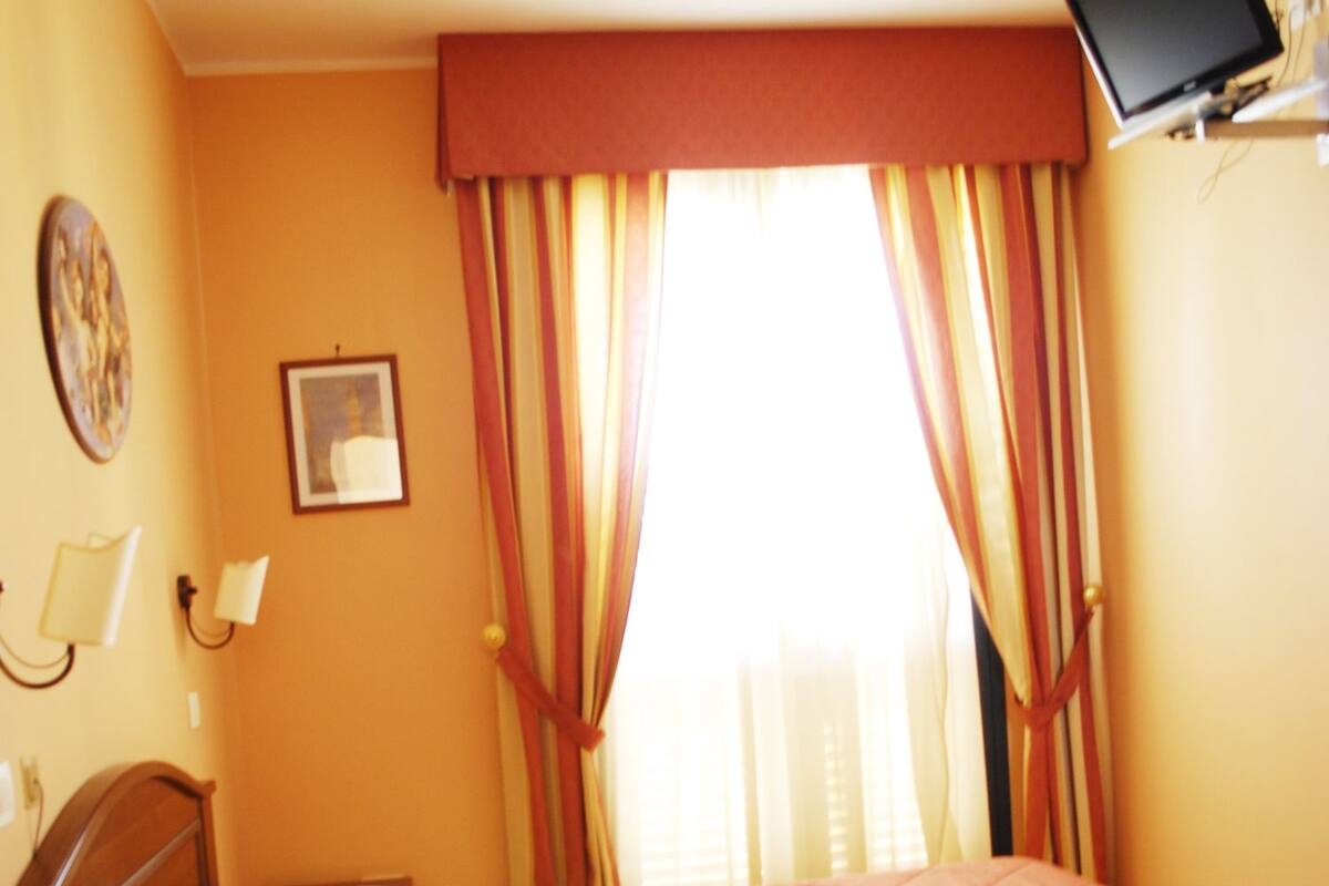 Une chambre d’hôtel avec un lit, un téléviseur fixé au mur et des rideaux.