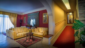 Een woonkamer met een gele zithoek, een rode vloerbedekking op de trap en een grote spiegel met een decoratieve lijst.