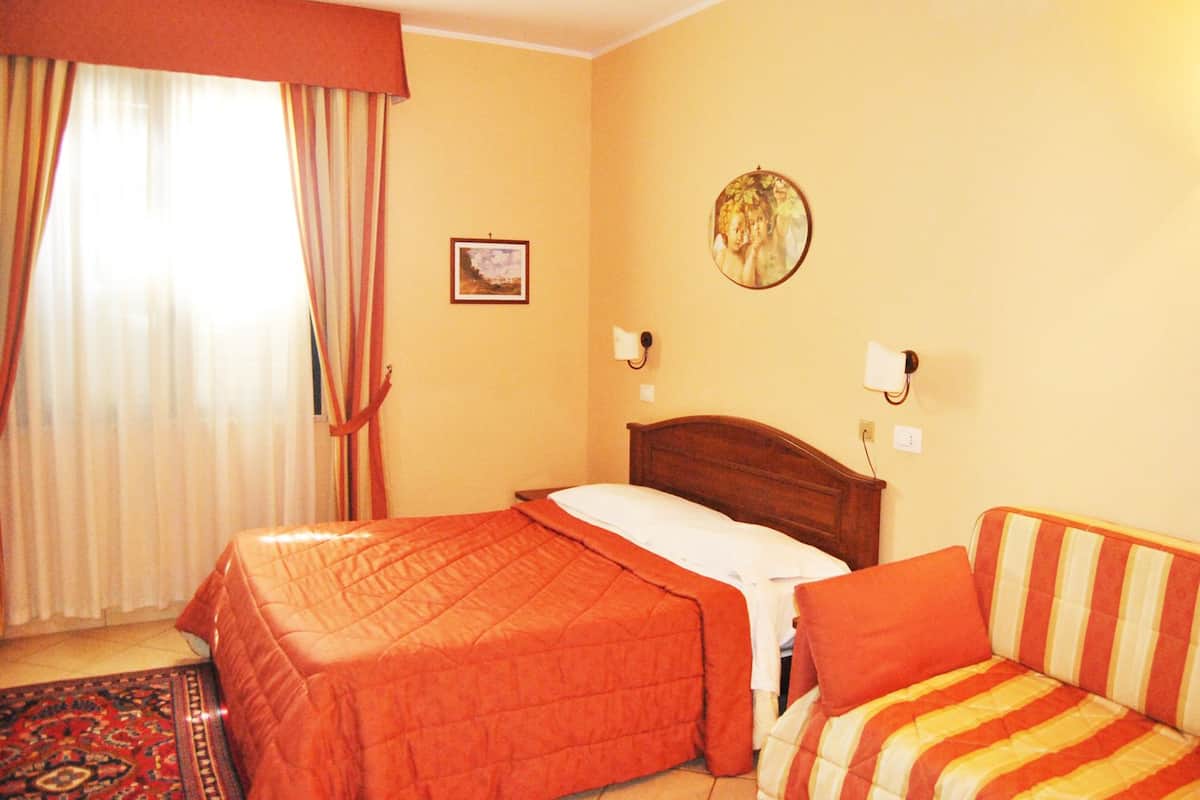 Une chambre d’hôtel avec un lit, un canapé, une fenêtre avec des rideaux, une horloge murale et un tableau encadré.