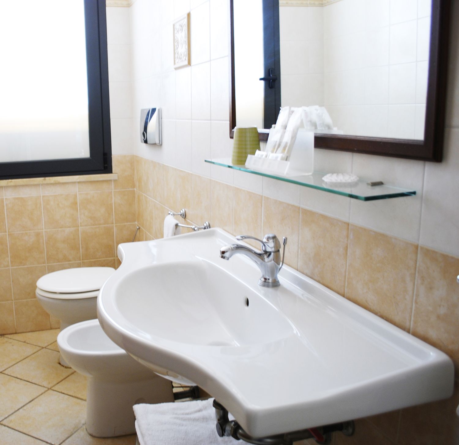 A bathroom with a sink, toilet, and a glass shelf above the sink.