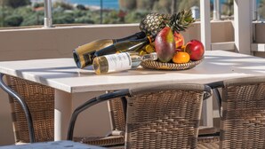 A balcony with wicker chairs, a table with a bottle of wine, a fruit bowl, and a view of mountains and a lake. - El Greco Apartments (Agios Nikolaos)