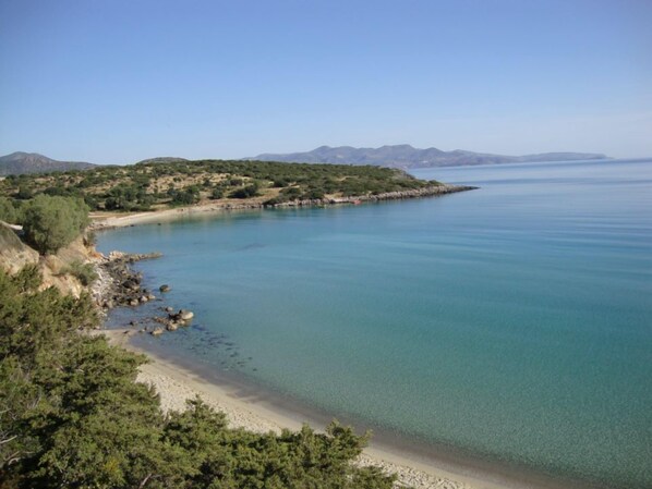 A coastal landscape with a clear view of the sea, a sandy beach, and a rocky shoreline.