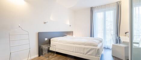 A modern bedroom with a bed, a bedside table, a hanging rack, and a bathroom with a mirror and sink.