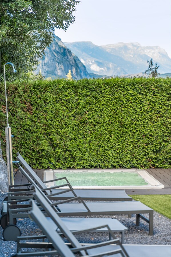 Zona de piscina con sillones de descanso y una fuente de agua, con montañas al fondo.