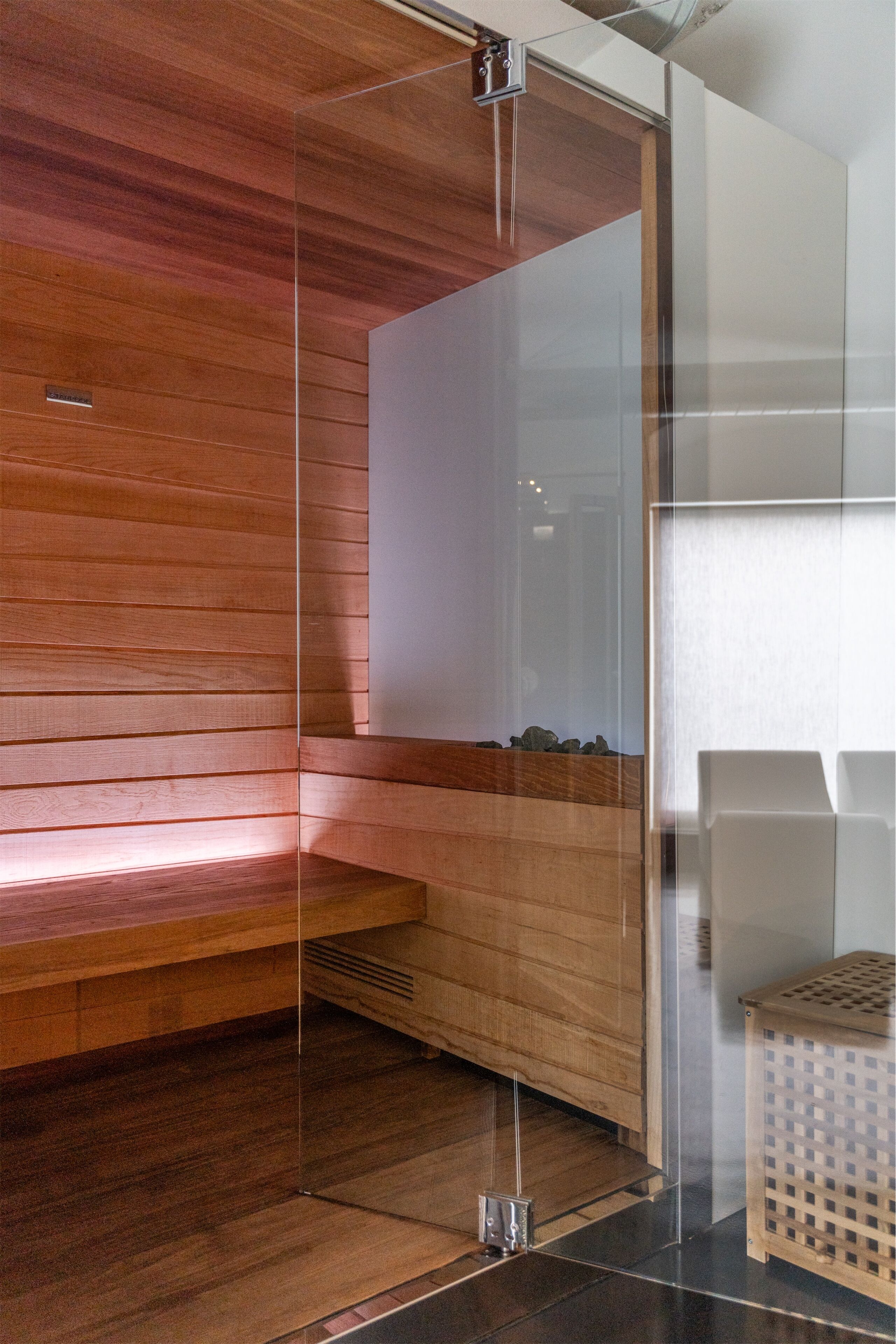 Una habitación moderna con un banco de madera, una división de vidrio y un pequeño taburete de madera.