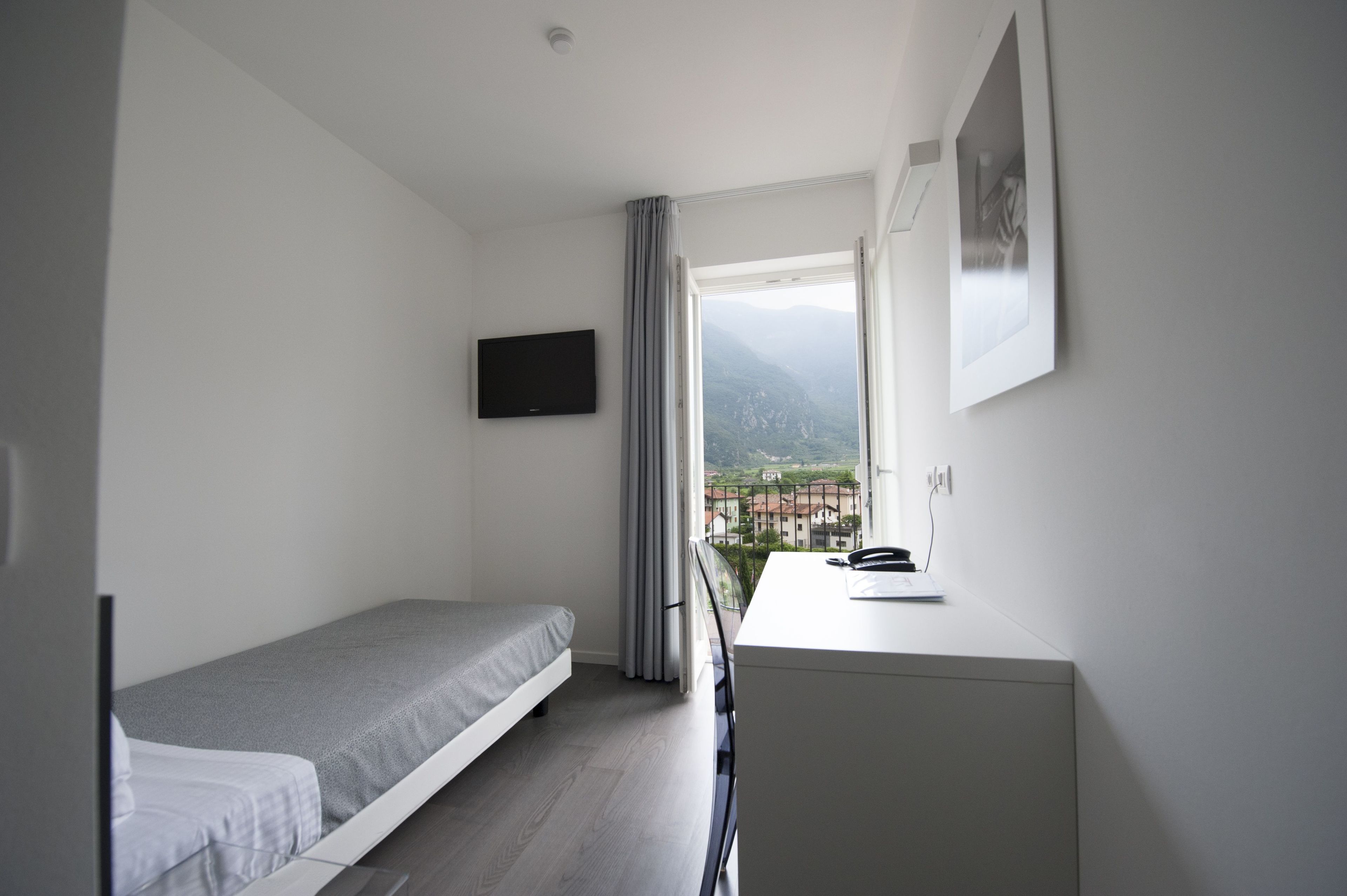 A small, modern room with a bed, a desk, a TV, and a window with a view of mountains.