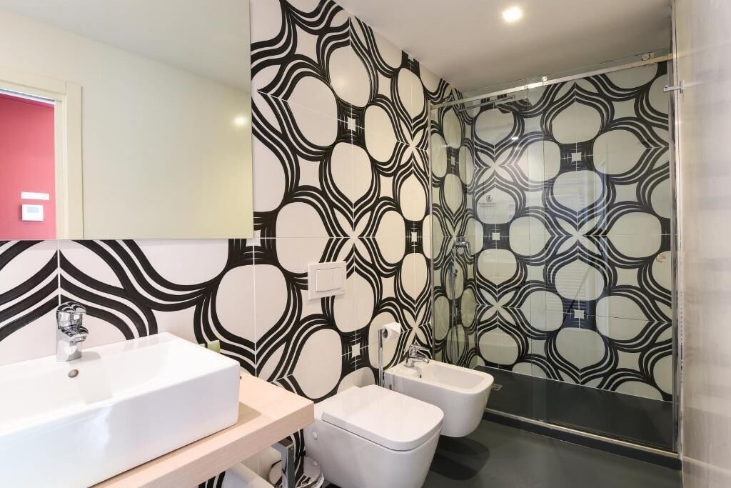Een moderne badkamer met een grote spiegel, een wit wastafel, twee witte toiletbrillen en een behang met patroon.