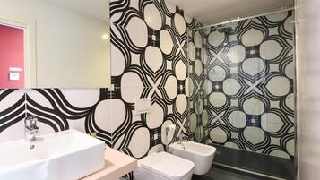 Een moderne badkamer met een grote spiegel, een wit wastafel, twee witte toiletbrillen en een behang met patroon.