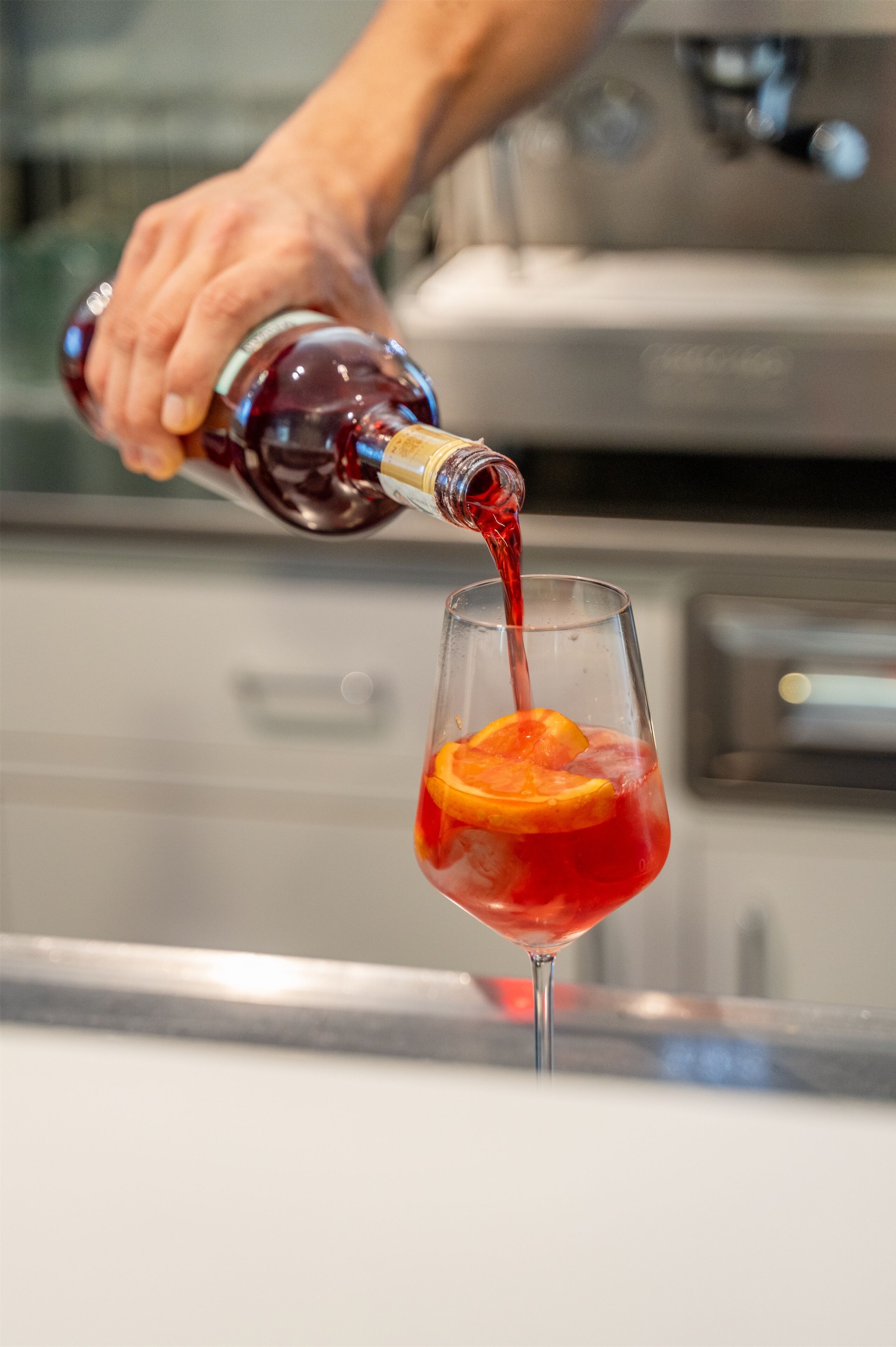 Una mano vertiendo un líquido rojo en un vaso con una rodaja de naranja.
