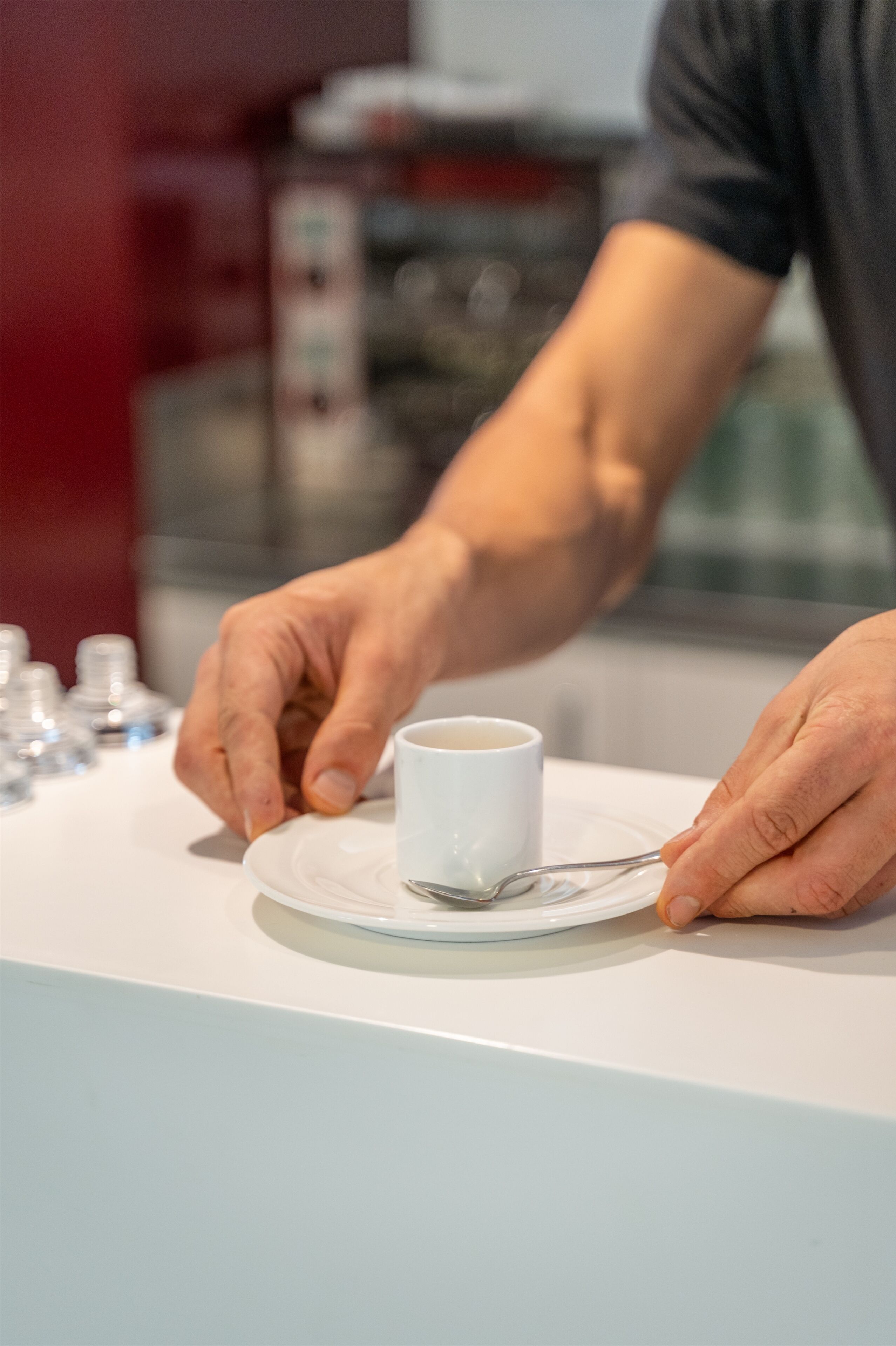 A person holding a spoon over a cup on a white plate.