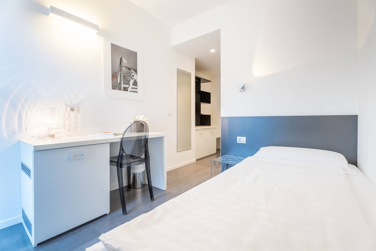Ein modernes Hotelzimmer mit weißem Schreibtisch, einem Sessel, einem Bett und einer blauen Akzentwand.