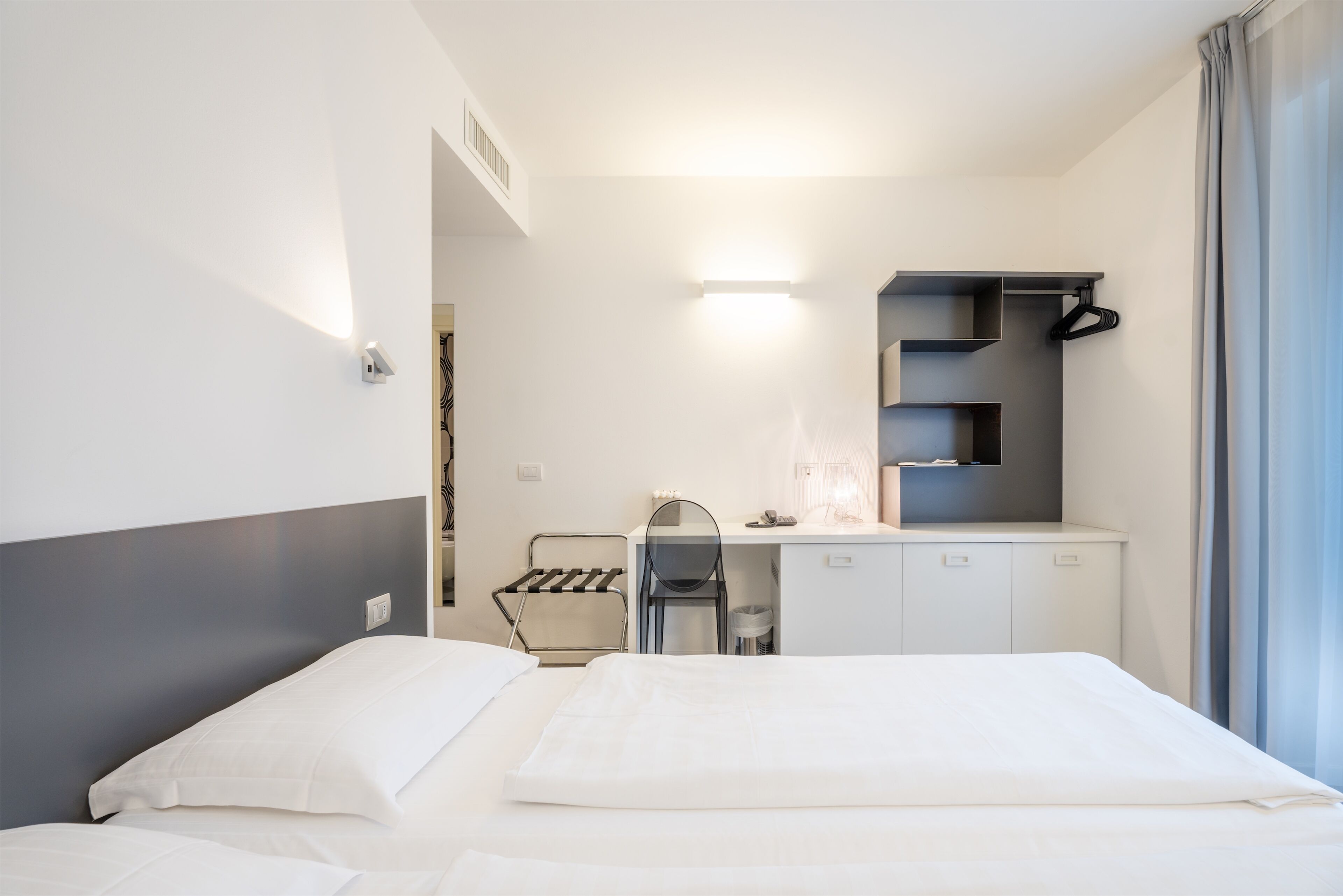 Une chambre d’hôtel équipée d’un lit, d’un bureau, d’une chaise, d’un porte-vêtements et d’une fenêtre avec des rideaux.