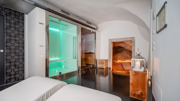 A modern hotel room with a glass-enclosed shower, a wooden side table with a candle, and a stone fireplace. - Garnì On The Rock (Arco)