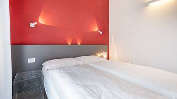 A hotel room with a bed, a small bedside table, and a red accent wall with lighting.