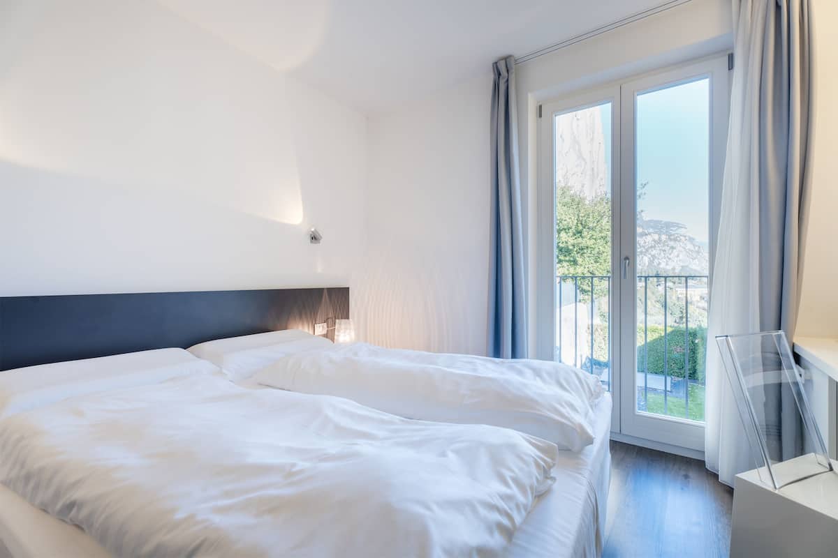 Ein modernes Hotelzimmer mit einem großen Bett, einem Nachttisch und Blick ins Freie durch eine Schiebetür.