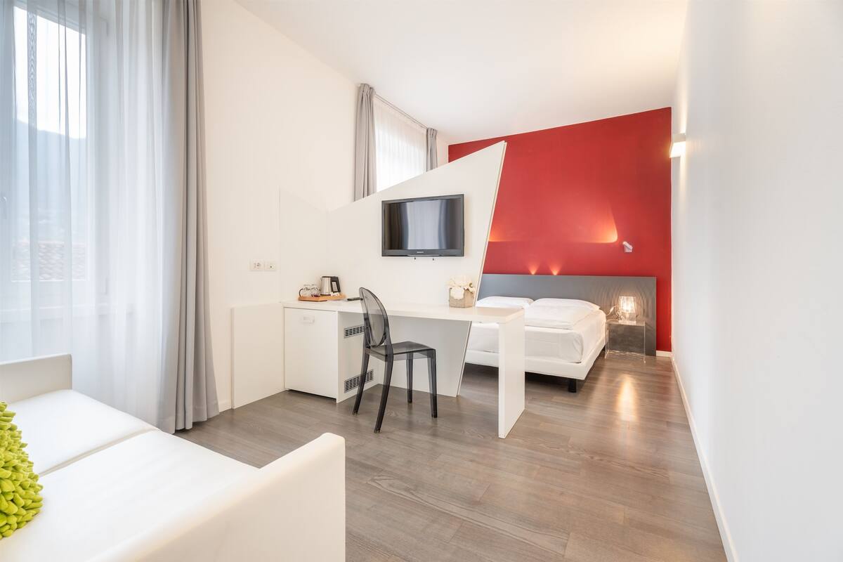 Ein modernes Hotelzimmer mit weißem Schreibtisch, Flachbildfernseher, Bett und einer Wand in Rot.