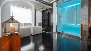 A modern bathroom with a glass-enclosed shower, a white bathtub, and a wooden side table with a candle. - Garnì On The Rock (Arco)