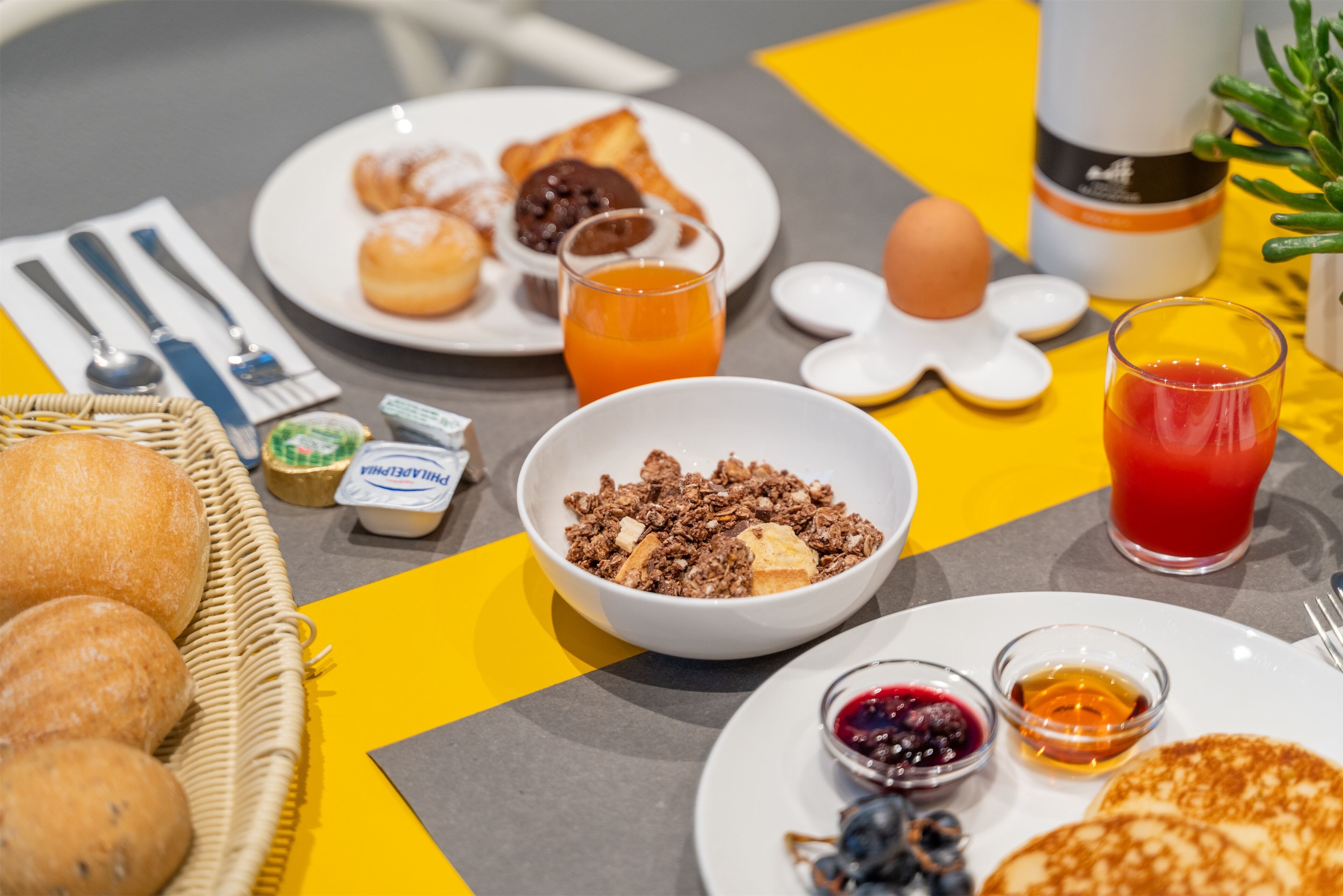 Ein Frühstückstisch mit verschiedenen Speisen, darunter Gebäck, eine Schüssel Müsli und Getränke.
