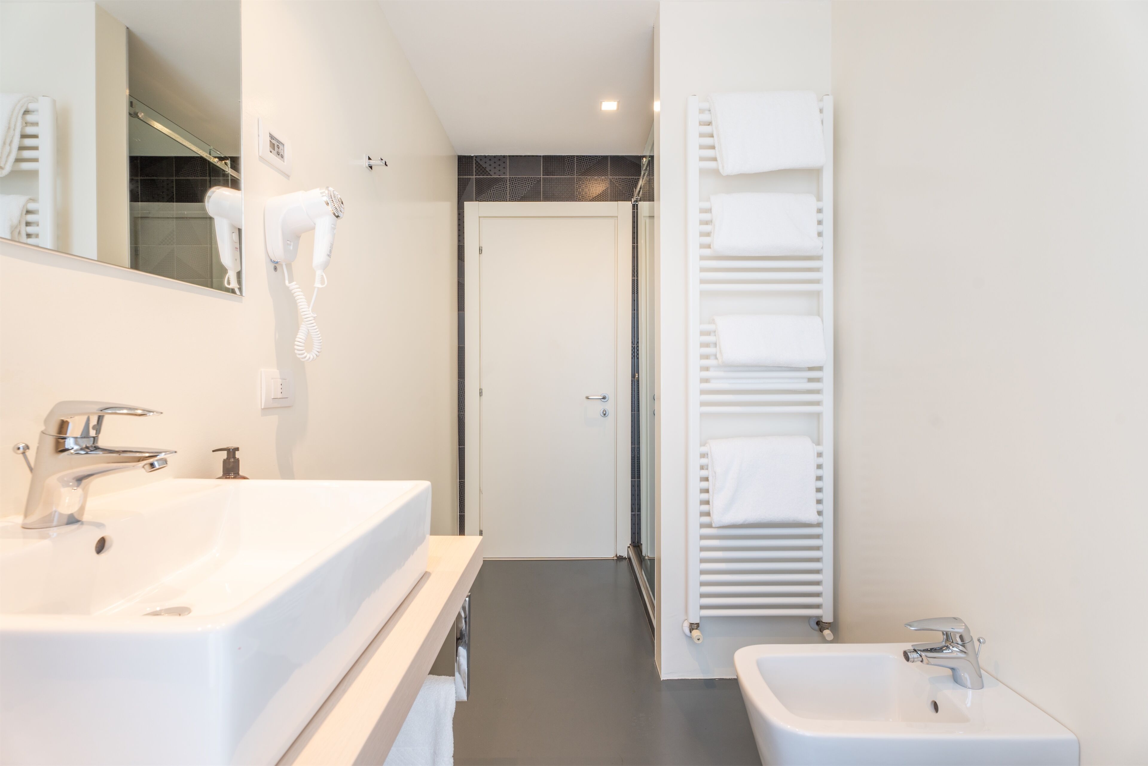 A modern bathroom with two sinks, a hairdryer, a towel rack, and a shower area.