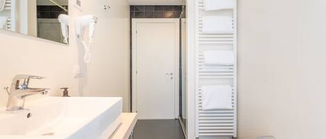 A modern bathroom with two sinks, a hairdryer, a towel rack, and a shower area.