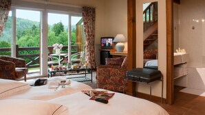A hotel room with a large bed, a desk with a computer, a chair, a balcony with a table and chairs, and a TV. - Hotel Neuhauser (La Broque)