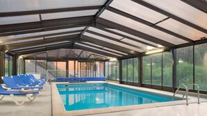 An indoor swimming pool with blue lounge chairs and a glass ceiling. - Hotel Neuhauser (La Broque)