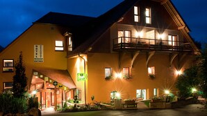 A two-story hotel with a balcony, illuminated windows, and a sign indicating a restaurant. - Hotel Neuhauser (La Broque)